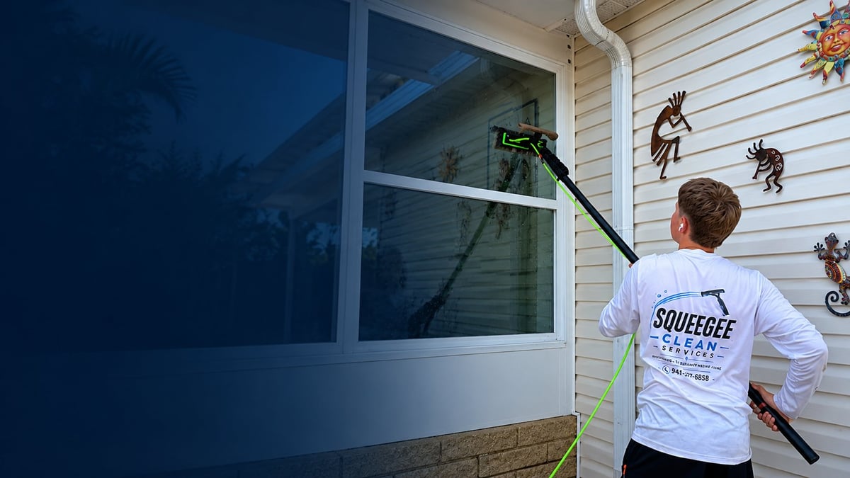 Owner of Squeegee Clean Services cleaning a home's window with a water-fed pole, wearing a branded Squeegee Clean Services shirt
